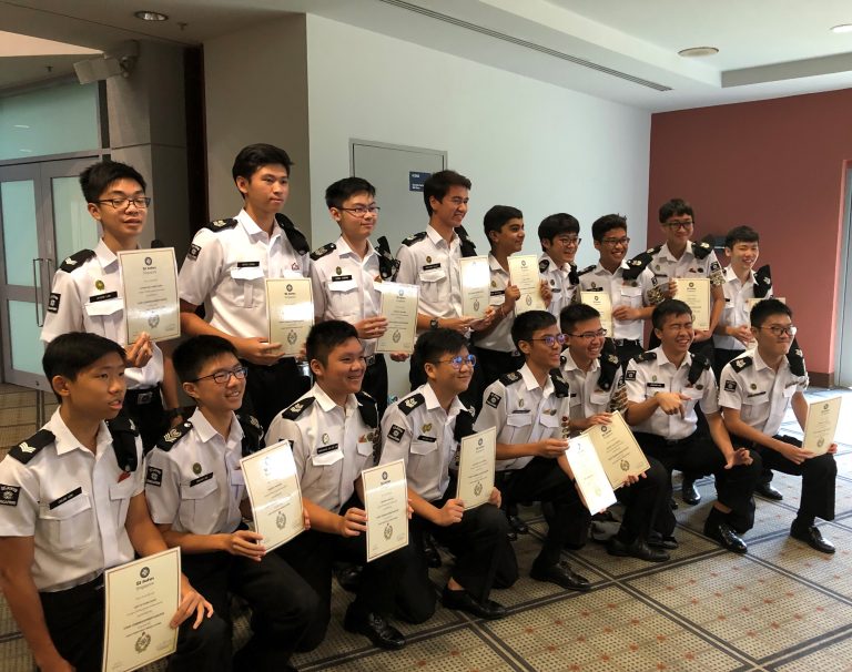 ACS(I) St John's Brigade members in white uniforms receive certificates or awards during a brigade prize presentation ceremony.